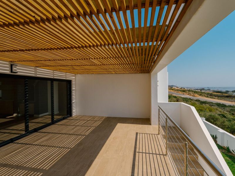 Spacious covered balcony featuring a timber slat pergola, tiled flooring, and a stainless steel balustrade with expansive coastal views.