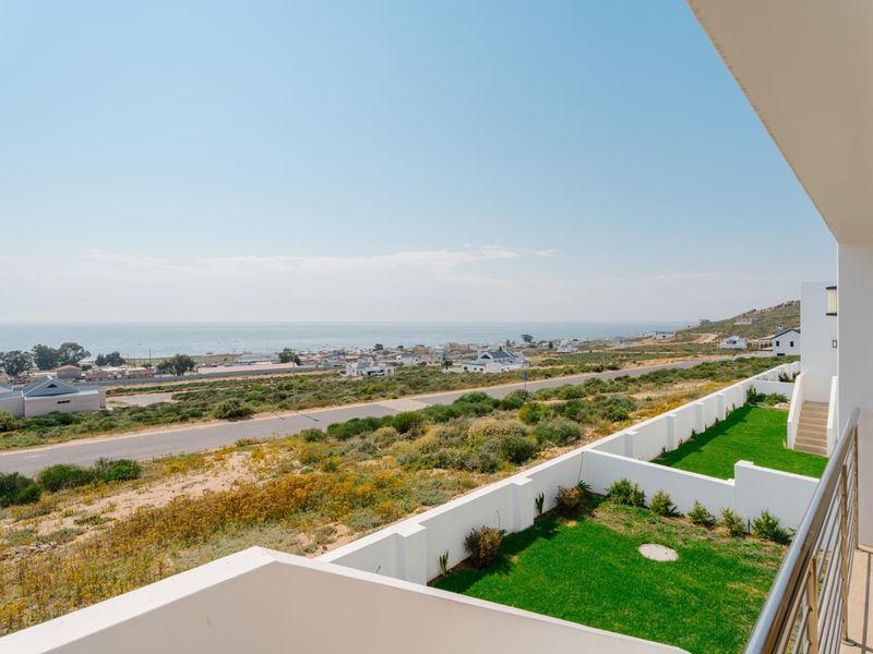 Elevated coastal view overlooking the surrounding landscape, residential area, and ocean from a modern balcony with clean white retaining walls and manicured lawn.
