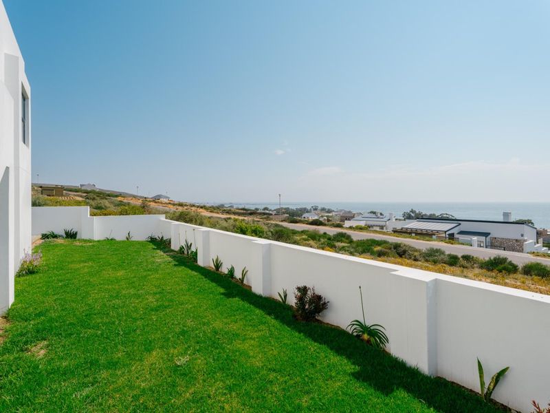 A well-maintained rear garden featuring a manicured lawn and a clean white boundary wall, offering scenic coastal views.