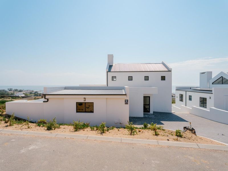 Modern white coastal house featuring a corrugated metal roof, paved driveway, and clean architectural lines with a view of the surrounding landscape.