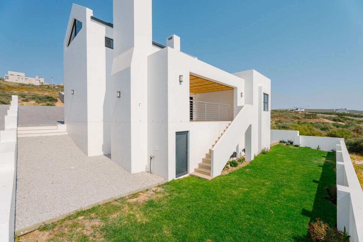 Rear view of a modern white house featuring an external staircase leading to a balcony with a timber pergola and a landscaped garden.