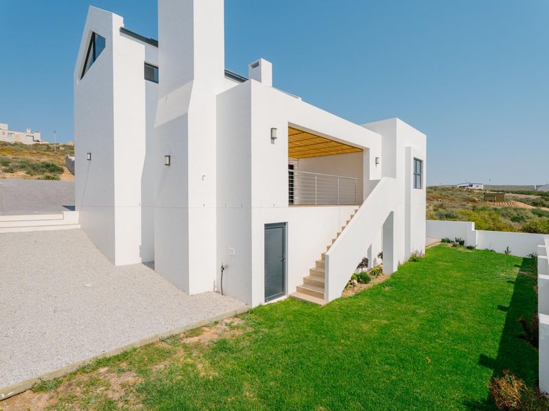 Rear view of a modern white house featuring an external staircase leading to a balcony with a timber pergola and a landscaped garden.