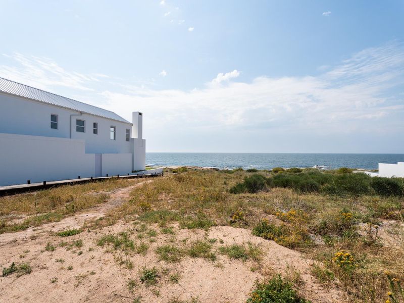 A view of the rear exterior of a coastal property featuring a wooden boardwalk leading towards the ocean.