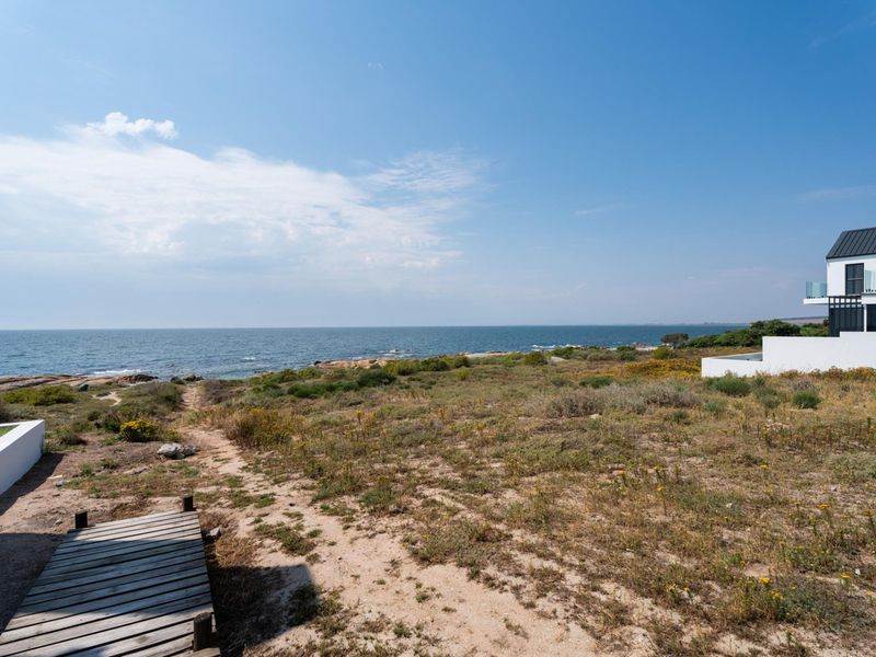 A scenic coastal view overlooking the ocean from a vacant residential plot featuring a wooden boardwalk and natural vegetation.
