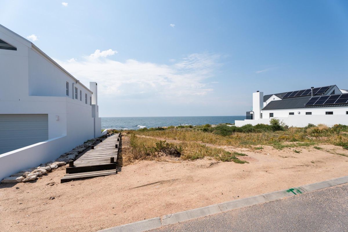 A scenic view of the coastline featuring a wooden boardwalk leading towards the ocean, flanked by modern residential properties.