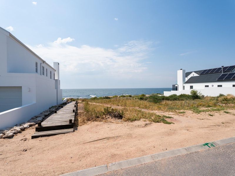 A scenic view of the coastline featuring a wooden boardwalk leading towards the ocean, flanked by modern residential properties.
