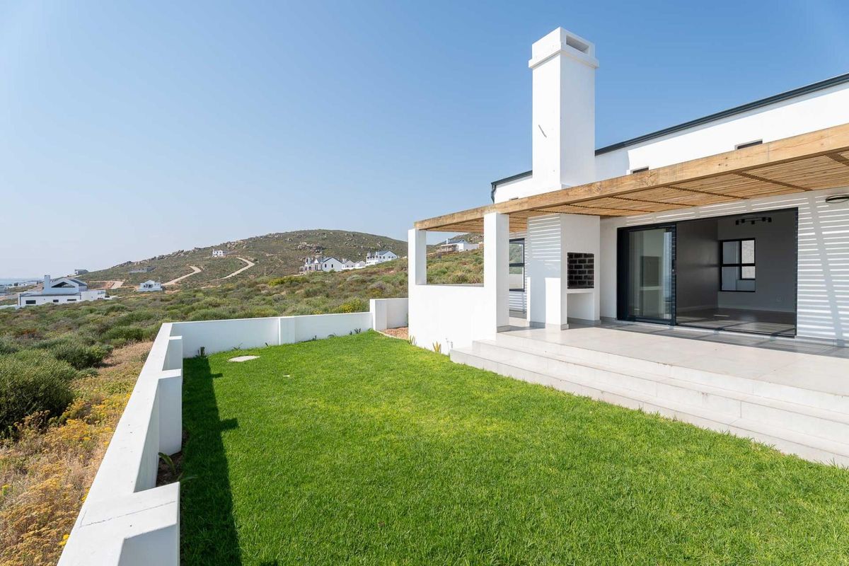 Rear exterior view featuring a tiled patio with a timber pergola, built-in braai, and a well-maintained lawn with surrounding boundary walls.