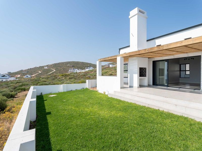 Rear exterior view featuring a tiled patio with a timber pergola, built-in braai, and a well-maintained lawn with surrounding boundary walls.