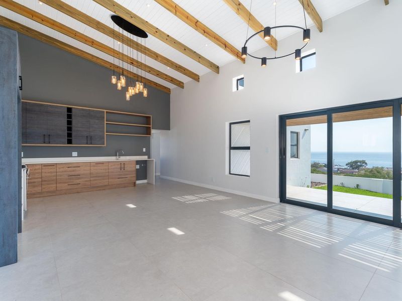 Spacious open-plan living area featuring vaulted ceilings with exposed timber beams, modern built-in cabinetry, and large sliding doors opening to a scenic coastal view.