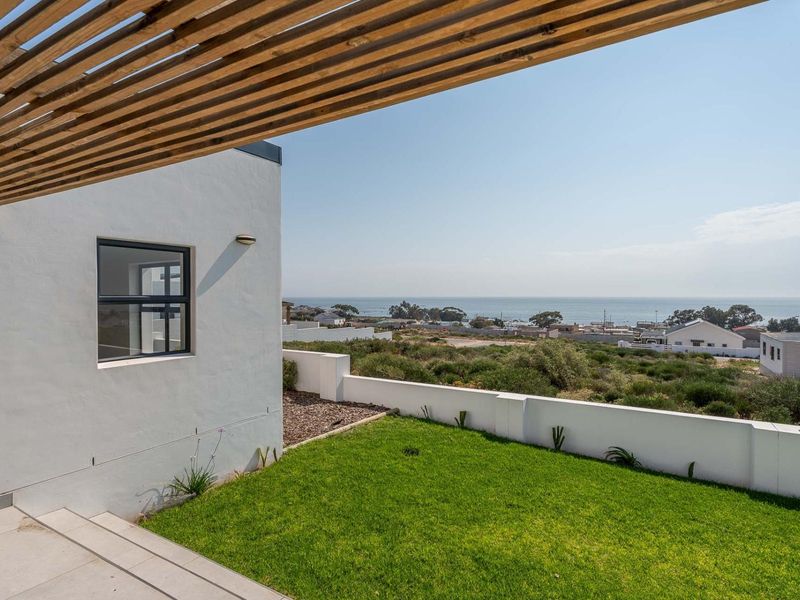 A modern patio area featuring a timber pergola, tiled flooring, and a low boundary wall, offering scenic coastal views.