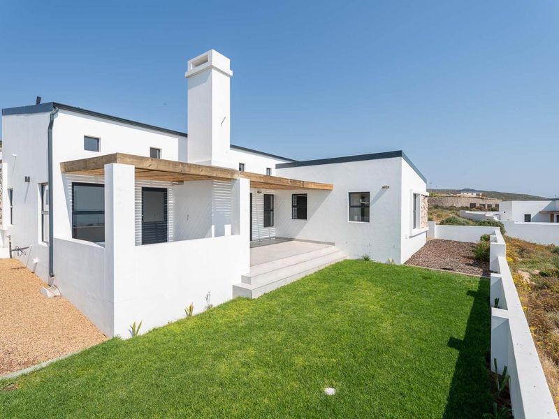 Rear view of a modern white house featuring a timber pergola over a concrete patio, overlooking a well-maintained lawn and boundary wall.