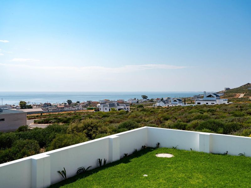Elevated coastal view overlooking the surrounding neighborhood and ocean, featuring a manicured lawn and a clean white boundary wall.