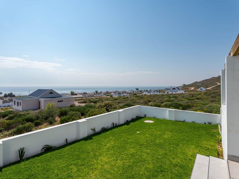 A scenic elevated view overlooking the coastal landscape, featuring a manicured lawn, white boundary wall, and a timber pergola structure.