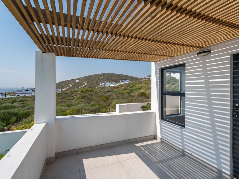 A modern covered balcony featuring a timber pergola, tiled flooring, and a masonry balustrade, offering scenic views of the surrounding landscape.