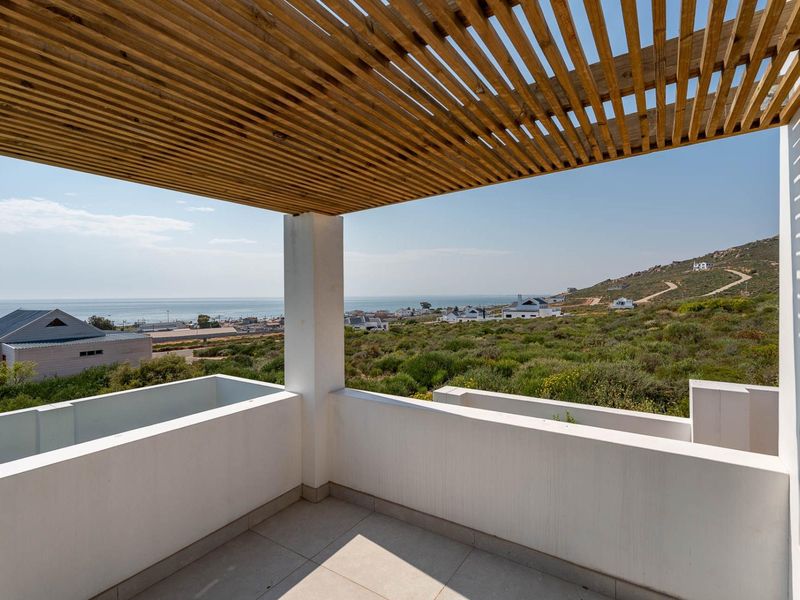 A modern balcony featuring a timber slat pergola, tiled flooring, and a masonry balustrade, offering expansive coastal and landscape views.