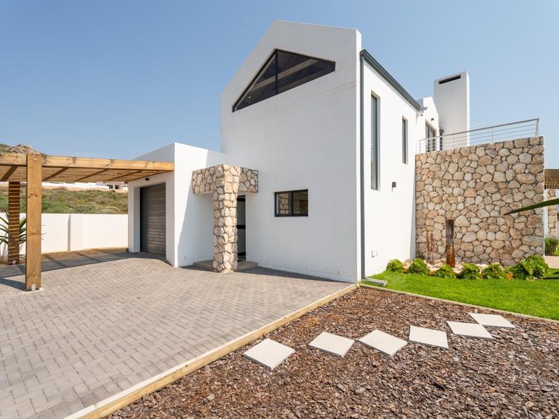 Modern architectural home featuring stone cladding, a timber pergola, paved driveway, and a clean white facade with a prominent chimney.