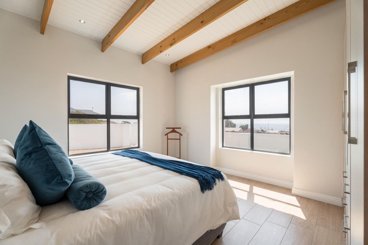 Bright bedroom featuring exposed timber ceiling beams, modern timber-look tiled flooring, built-in wardrobes, and large windows with views.