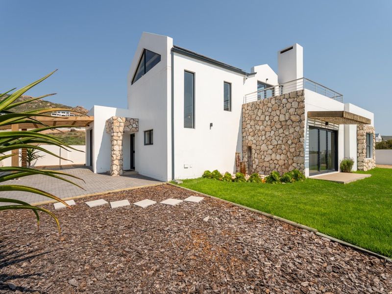Modern architectural home featuring stone cladding, clean white facade, paved driveway, and a balcony with a timber pergola.