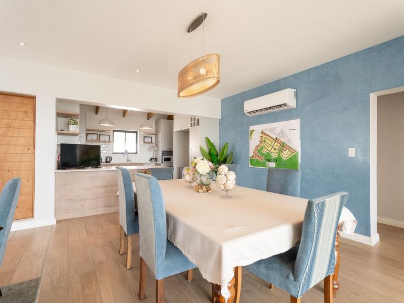 Bright open-plan dining and kitchen area featuring wood-look tile flooring, modern pendant lighting, a split-system air conditioner, and a functional kitchen with subway tile backsplash.