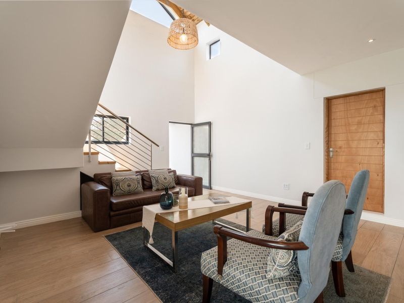 Bright living area featuring high vaulted ceilings with a skylight, modern staircase, and light wood-look flooring.