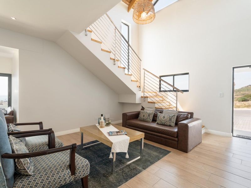Bright, modern living area featuring a striking staircase with timber treads, stainless steel balustrade, exposed rafters, and a skylight, opening to the outdoors.