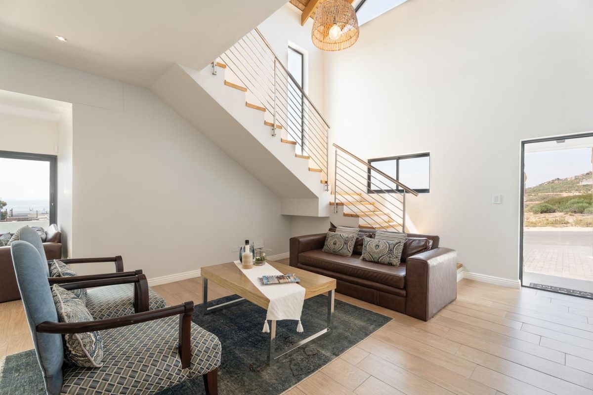 Bright, modern living area featuring a striking staircase with timber treads, stainless steel balustrade, exposed rafters, and a skylight, opening to the outdoors.