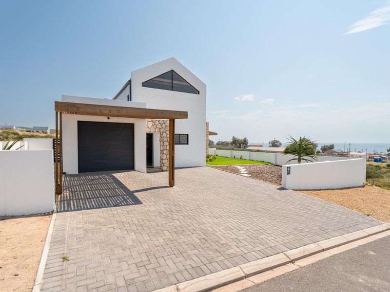 Modern coastal home featuring a paved driveway, timber pergola, garage, and distinctive triangular gable window with stone facade accents.