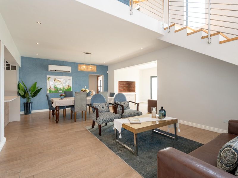 Spacious open-plan living and dining area featuring wood-look tile flooring, recessed lighting, and a modern staircase with a stainless steel balustrade.