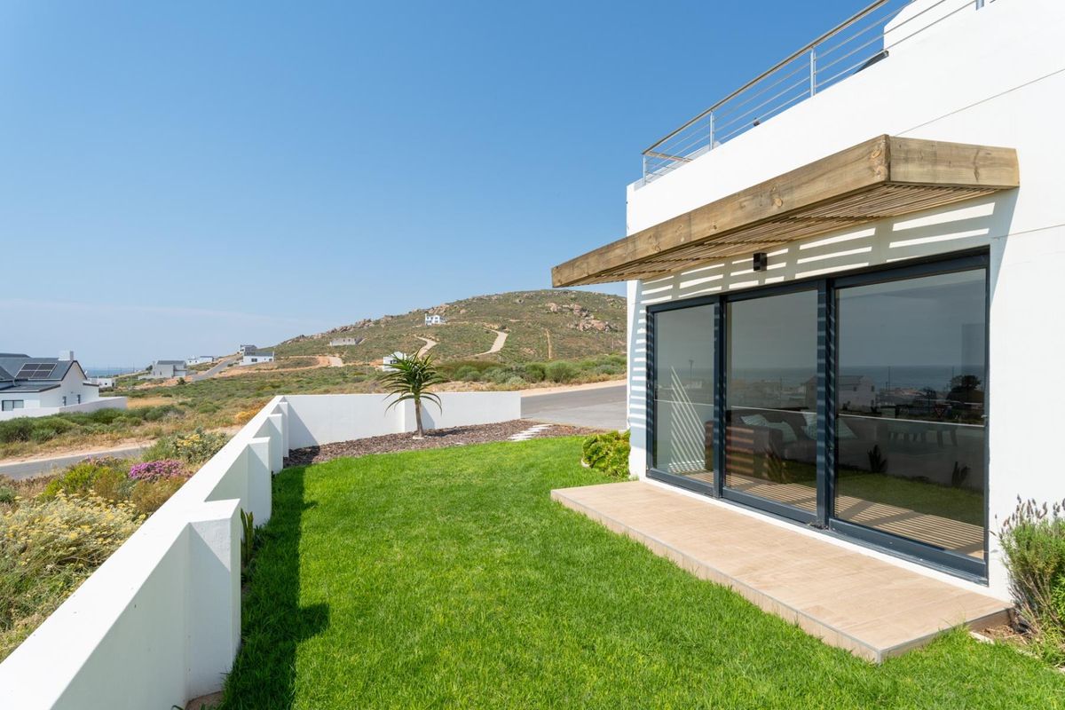A modern rear exterior view featuring a tiled patio, timber pergola, sliding glass doors, and a well-maintained garden with a boundary wall.