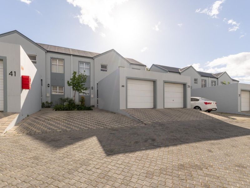 Front elevation of a residential townhouse complex featuring paved driveways, multiple garage units, and modern grey exterior finishes.