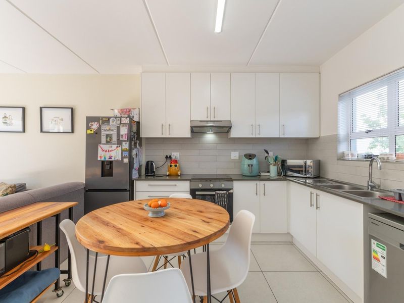 An open-plan kitchen featuring white cabinetry, a tiled backsplash, and integrated appliances, seamlessly flowing into the adjacent living and dining area.
