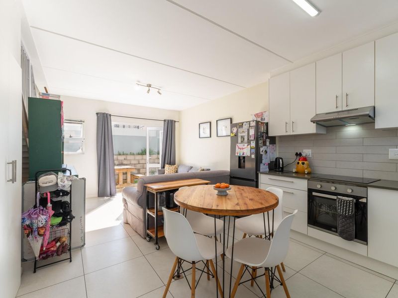 Open-plan living and kitchen area featuring modern white cabinetry, integrated appliances, tiled flooring, and direct access to an outdoor patio space.