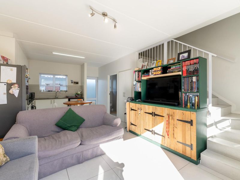 Open-plan living area featuring tiled flooring, a staircase with metal railing, and an integrated kitchen space with functional cabinetry and sink.