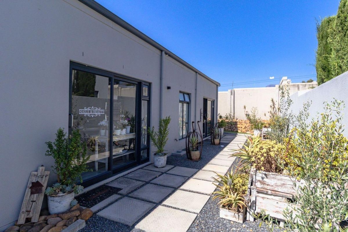 A well-maintained rear exterior view featuring a paved walkway, gravel landscaping, and modern sliding glass doors leading into the property.