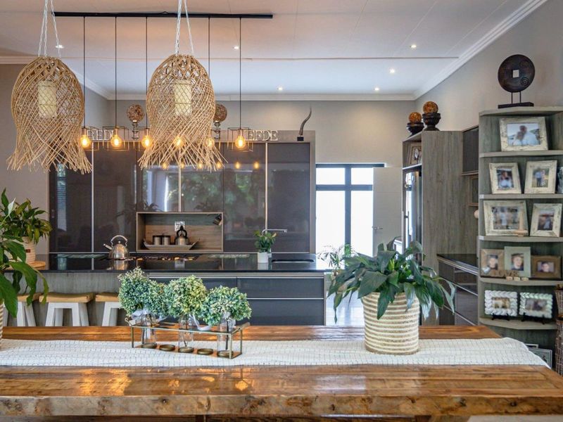 Spacious open-plan kitchen and dining area featuring modern dark cabinetry, stone countertops, a large kitchen island, and a textured stone feature wall.