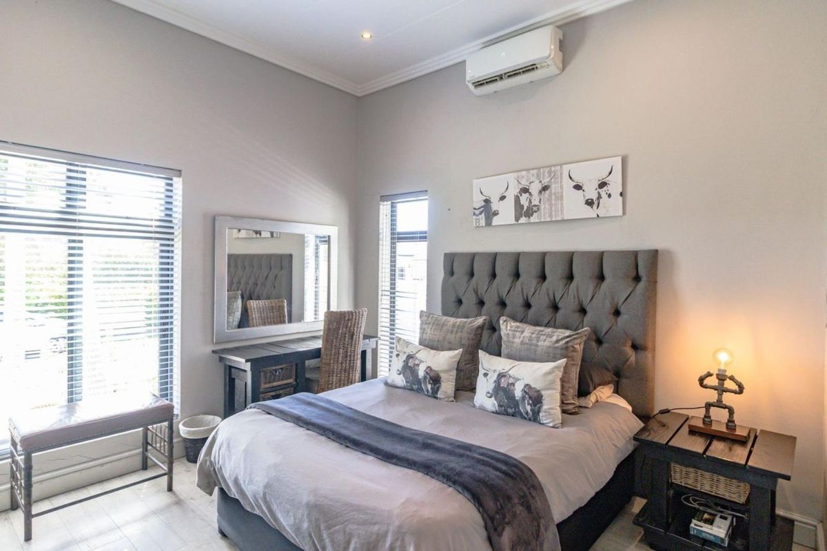A well-maintained bedroom featuring a split-system air conditioner, modern recessed lighting, and large windows with venetian blinds.