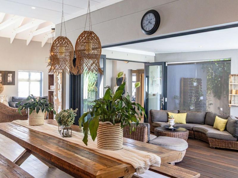 Spacious open-plan living and dining area featuring exposed timber rafters, seamless indoor-outdoor flow through bi-fold doors, and warm timber decking.