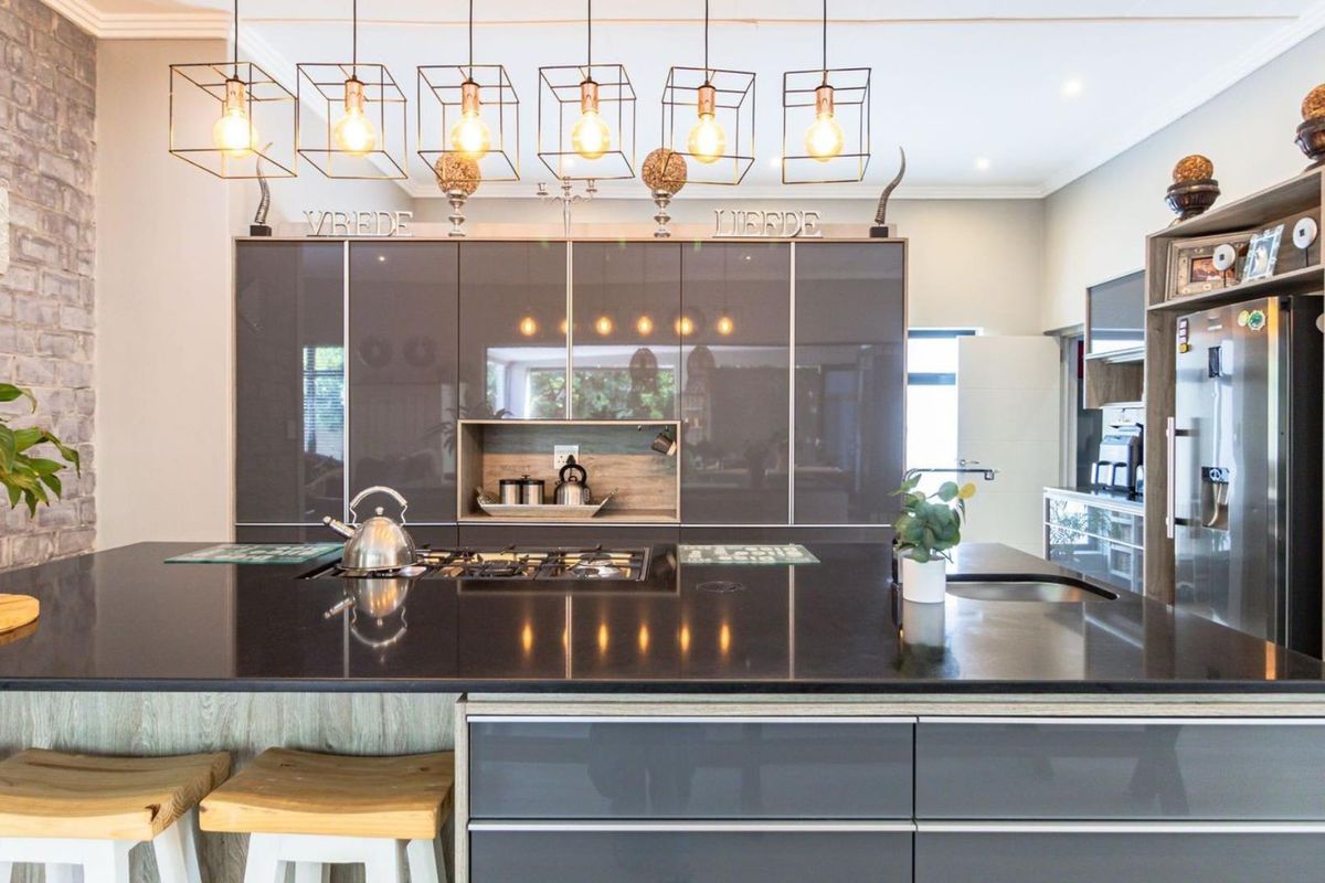 Modern kitchen featuring a large central island with a gas hob, sleek high-gloss cabinetry, and stylish pendant lighting against an exposed brick feature wall.