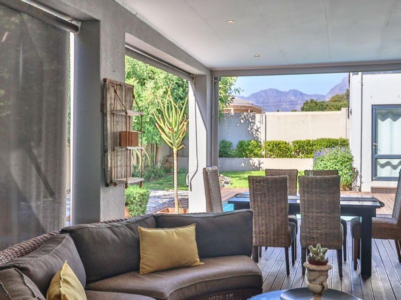 A spacious covered patio featuring timber decking, recessed lighting, and retractable blinds, offering a seamless transition to the garden and pool area.