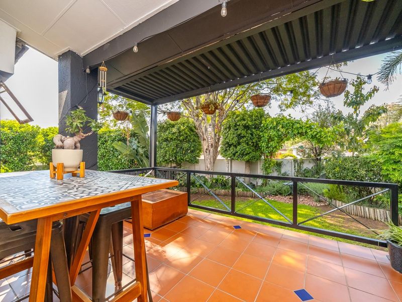 A well-maintained covered patio featuring tiled flooring, a black metal balustrade, and a pergola, overlooking a lush private garden.