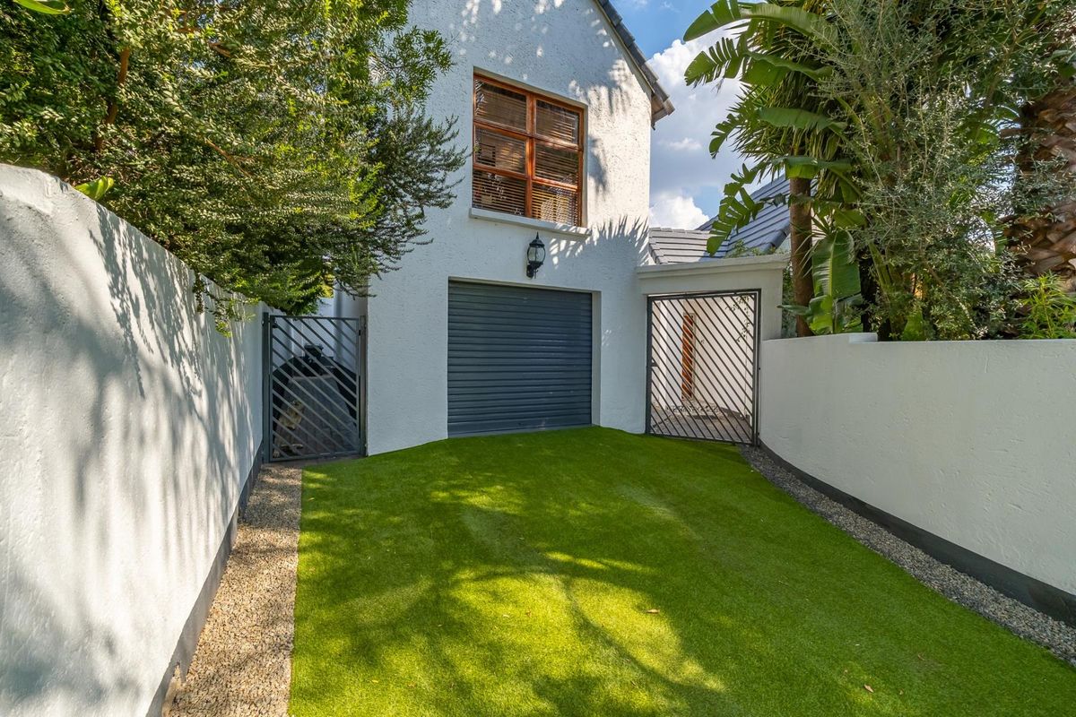 A well-maintained rear courtyard featuring artificial turf, secure metal gates, and access to the garage.