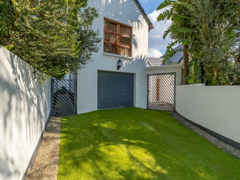 A well-maintained rear courtyard featuring artificial turf, secure metal gates, and access to the garage.