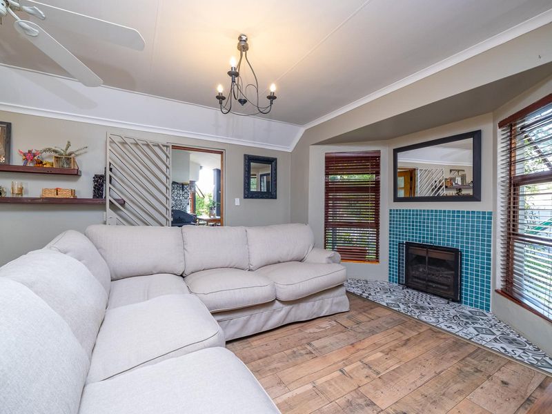 A cozy living room featuring timber flooring, a fireplace with decorative tiling, built-in shelving, and a ceiling fan.