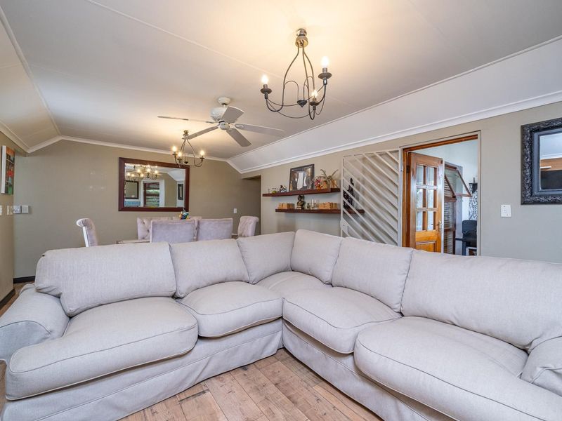 A comfortable living room featuring timber flooring, a ceiling fan, and decorative wall shelving, with an adjacent dining area visible.