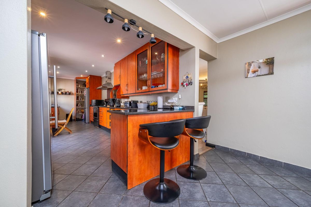 A functional kitchen featuring warm-toned wooden cabinetry, granite countertops, a breakfast bar, and tiled flooring, with an integrated pantry and built-in cooking appliances.