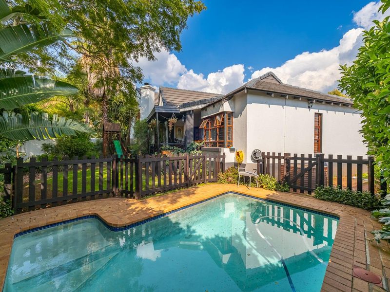 A well-maintained rear garden area featuring a swimming pool with brick coping, enclosed by a timber fence, adjacent to the home's covered patio.