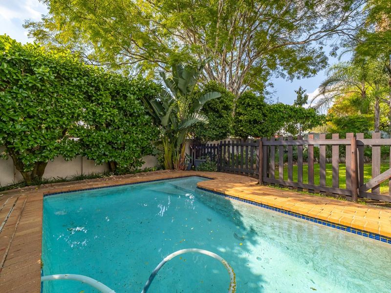 A private swimming pool area featuring brick coping, a timber fence, and established garden greenery.