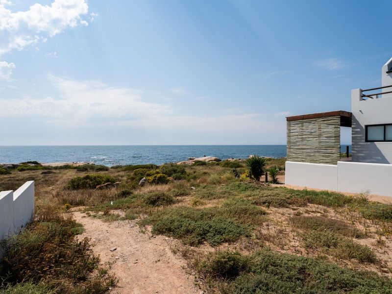 A view of the rear exterior of the property featuring a coastal landscape and a patio structure overlooking the ocean.