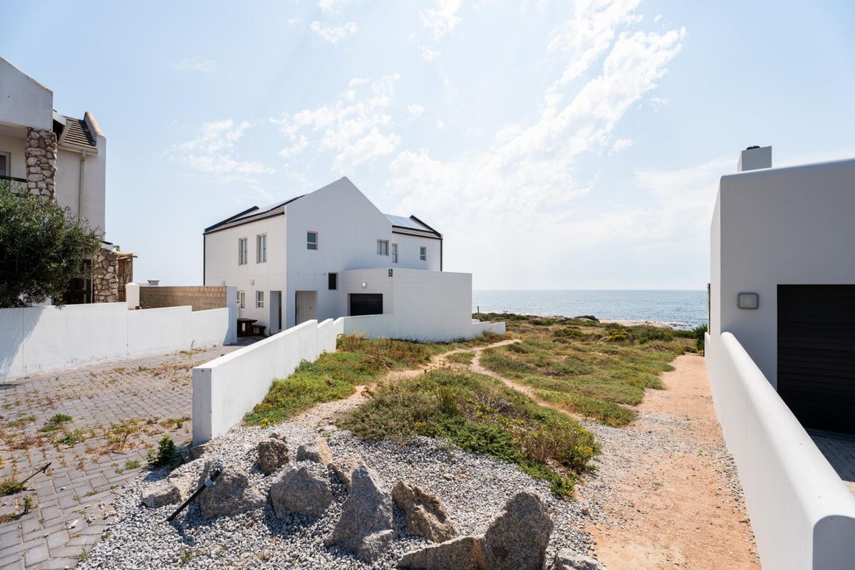 Rear view of a coastal residential property featuring a paved driveway, boundary walls, and direct access to the natural landscape and oceanfront.