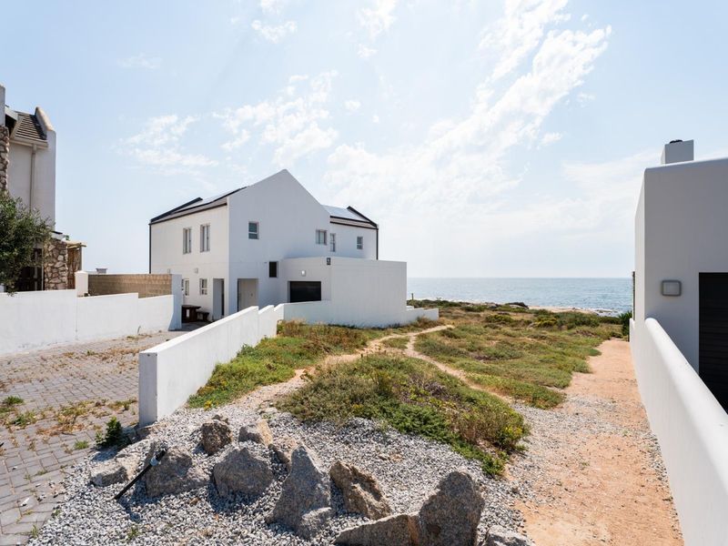 Rear view of a coastal residential property featuring a paved driveway, boundary walls, and direct access to the natural landscape and oceanfront.